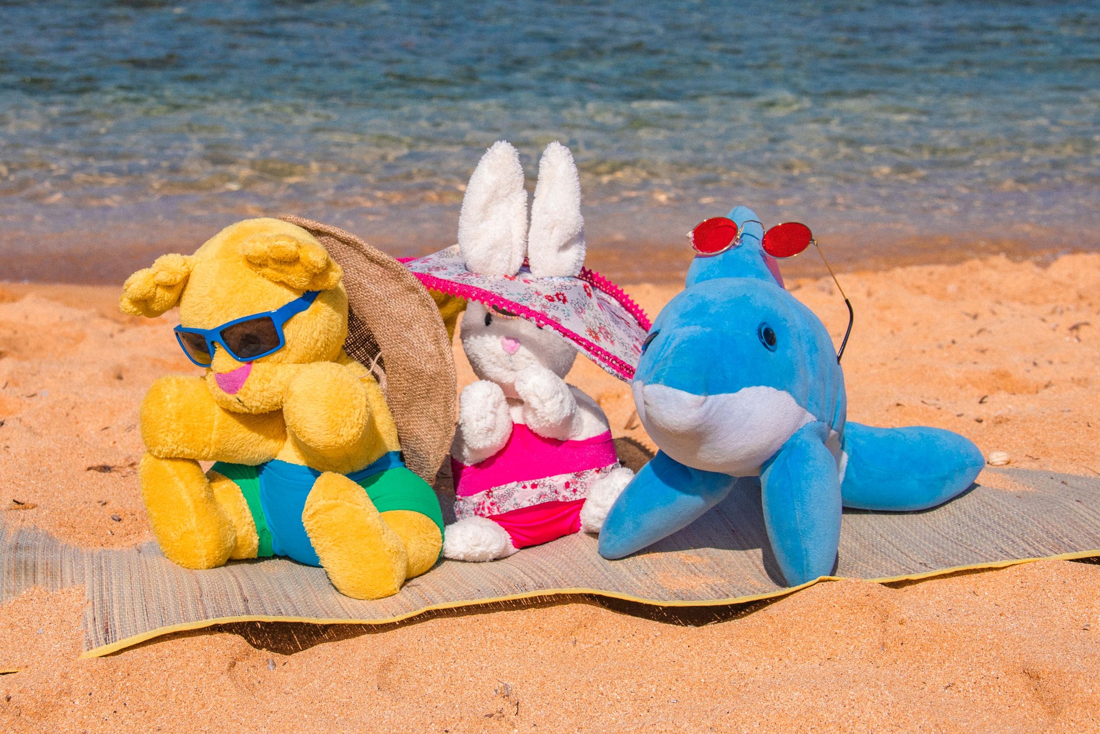 Drie knuffels liggen op een handdoek op het strand