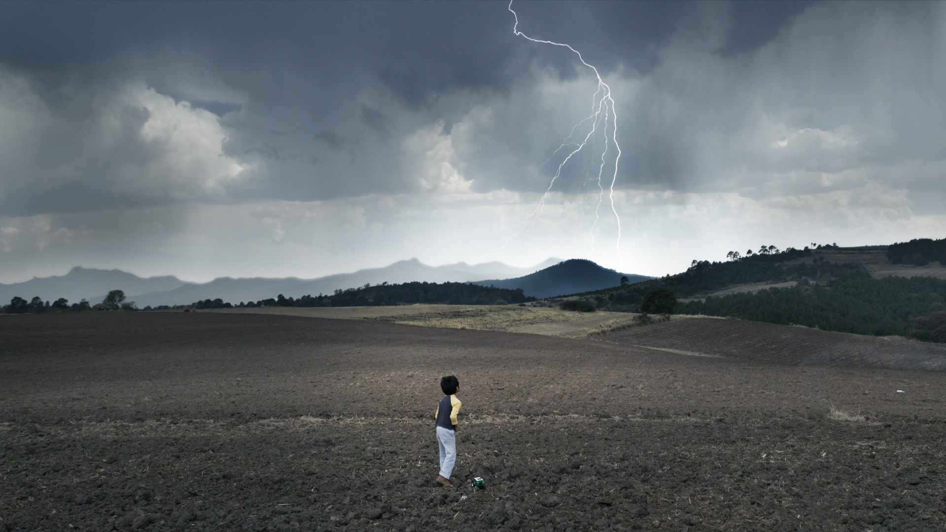 Een jongetje rent over een groot open veld met in de achtergrond een bliksemschicht in de luch