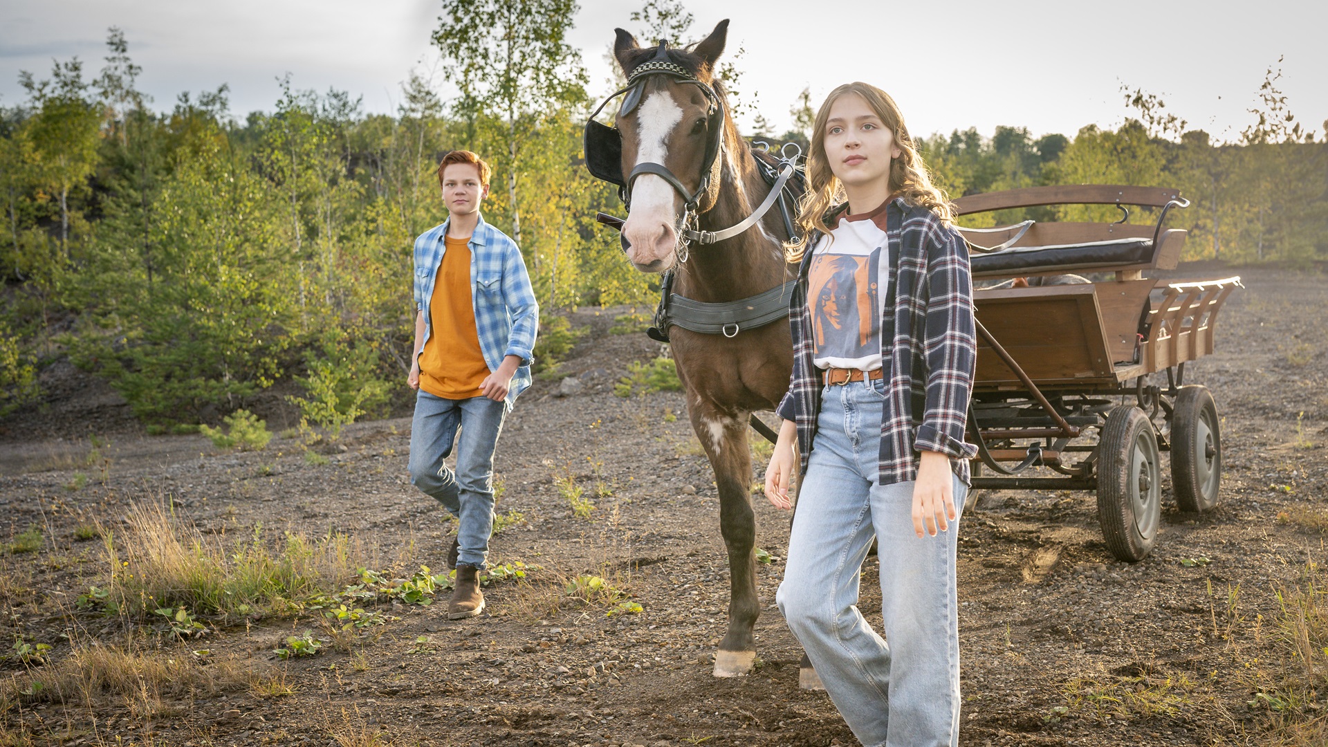 Een jongen en meisje lopen naast een paard en wagen
